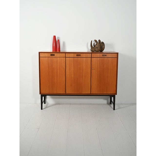Swedish highboard from the 1960s–70s in teak and dark lacquered oak, three drawers, three doors, original label. Swedish-...
