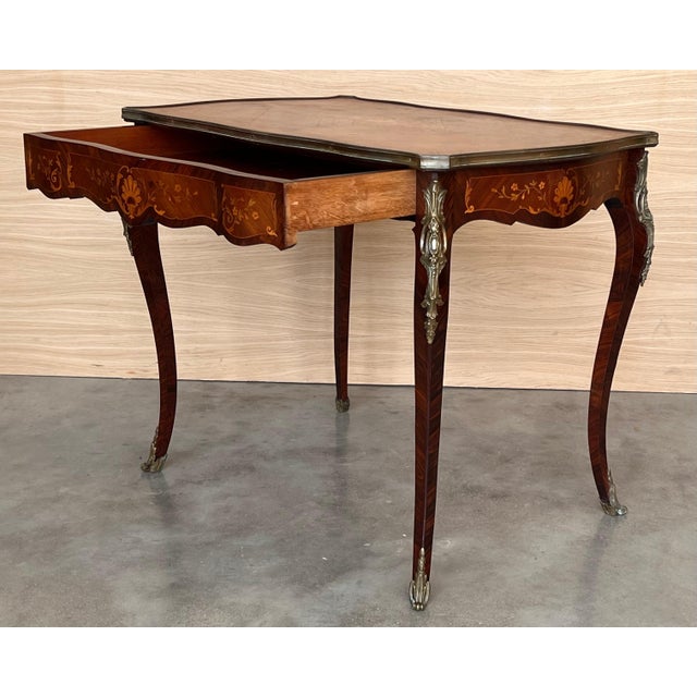 This beautiful marquetry writing table features a lovely brass banded serpentine top, bronze mounts, and one large drawer....