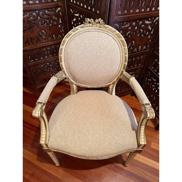 1940s–1950s large Louis XVI Revival armchair featuring an oval upholstered back topped with a carved ribbon-bow crest. The...