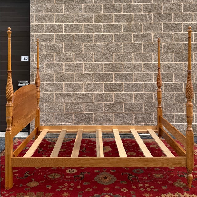 A vintage American Traditional solid oak queen poster bed having turned and twisted posts and finials, an arched panel...