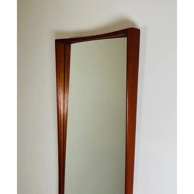An elegant teak wall mirror by Asbjorn-Mobler having a curved teak sculptural frame that brings the wall upon which it is...