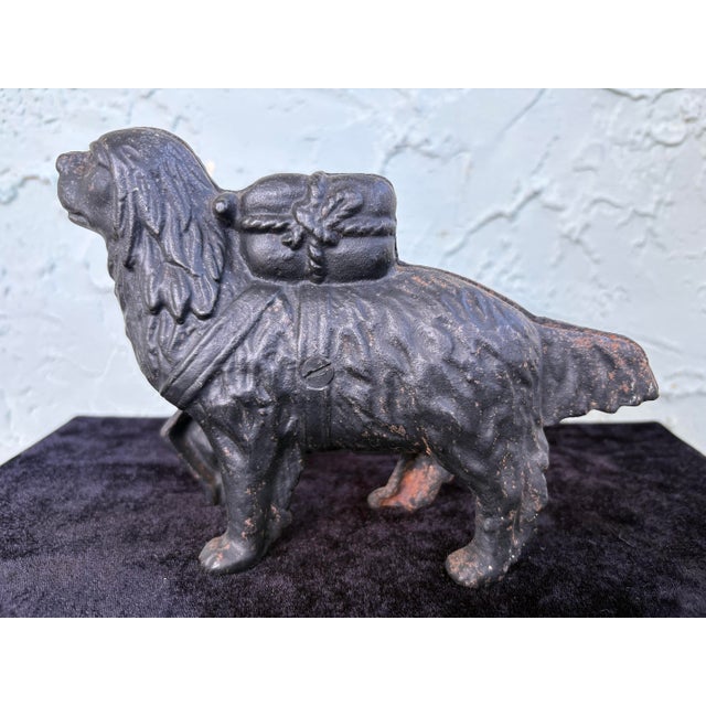 This charming antique cast iron still coin bank depicts a standing dog carrying saddle bags on its back, a classic and...
