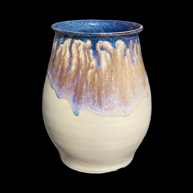 This handmade ceramic vase features a striking drip glaze design in shades of blue and brown flowing over a lighter cream-...