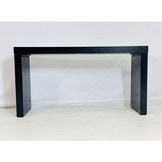 Architectural in form and understated in its elegance, this modern console table features a rich black cerused oak finish...