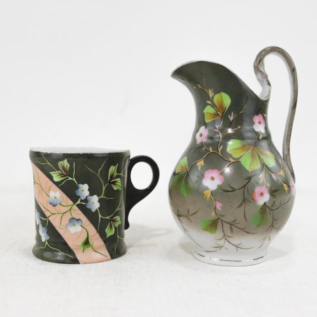This elegant vintage porcelain pitcher and cup set showcases a stunning hand-painted floral motif in soft pastel hues...