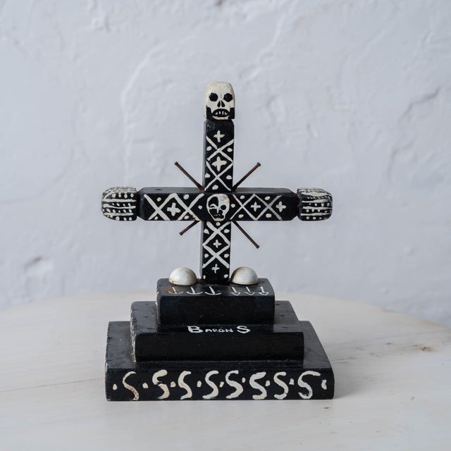 A Haitian Vodou cross for Baron Samedi, carved and painted black with white detailing, on a three-tier stepped base. A...