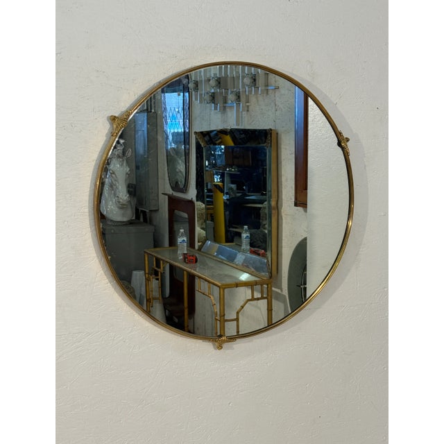 A round wall mirror featuring a slim brass frame accented with small decorative mounts at the top, sides, and bottom. Its...
