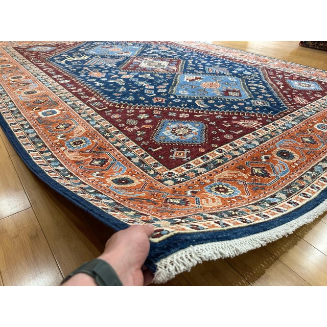 This handmade Qashqai-style rug features a vibrant tribal design with bold red, navy, and sky blue tones, inspired by...
