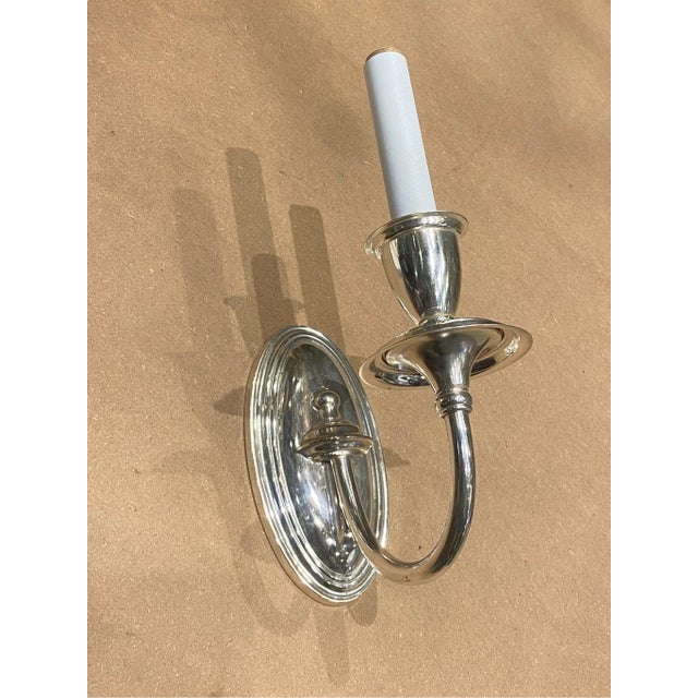 A classic single-arm wall sconce with a polished metal finish. Oval-shaped backplate with soft ridged detailing, providing...