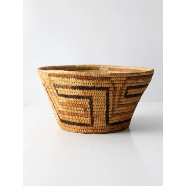 This is a vintage basket bowl. The handwoven woven basket features a decorative pattern in browns and black.