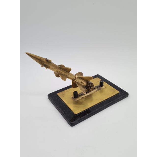 The Space Age-style rocket figurine, made of bronze with a subtle golden hue, represents the spirit of the modernist...