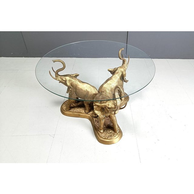 Hollywood regency brass elephant coffee table. The coffee table consists of a brass base featuring 3 brass elephants and a...