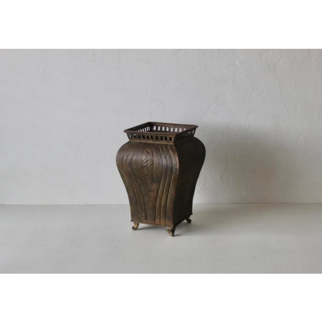 Vintage footed brass planter featuring an aged dark patina, an embossed leaf and fluted panel design, and a pierced square...