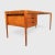 50 Hare teak desk with three drawers. The desk is in excellent condition. This piece is attributed to the mentioned...