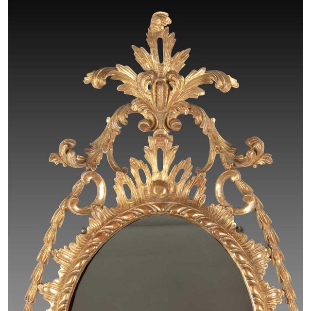 An exceptional quality mid C18th oval giltwood wall mirror, with elaborate overhanging scroll acanthus crest, above...