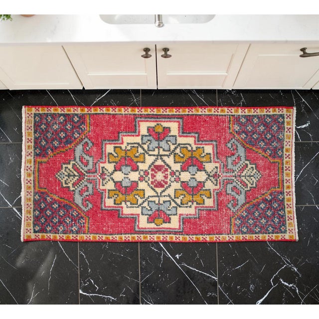 This charming vintage hand-knotted Oushak mat showcases a vibrant raspberry red field adorned with classic geometric...