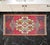 This charming vintage hand-knotted Oushak mat showcases a vibrant raspberry red field adorned with classic geometric...