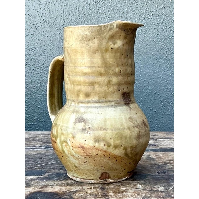 This stoneware jug embraces a classic, functional silhouette, its rounded, full-bellied body rising through a defined...