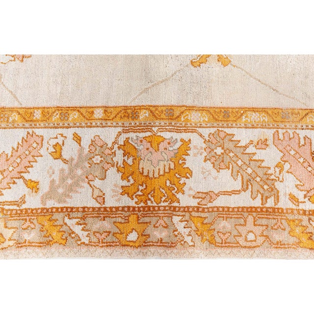 This antique Turkish Oushak rug rests on a softly mottled ivory-cream field shot through with very pale beige abrash....