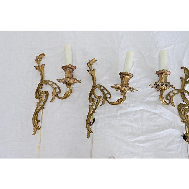An exceptional grouping of four early 20th century Louis XV-style wall sconces, made of gilt bronze sculpted into the most...