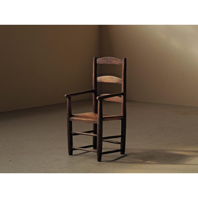 19th-century folk armchair with a woven rush seat and a backrest formed by three slightly curved rails. The uprights...