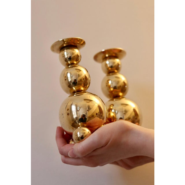 Made in Sweden. A pair of Swedish brass candle holders shaped like spheres and resting on three balled feet by GUSUM dated...