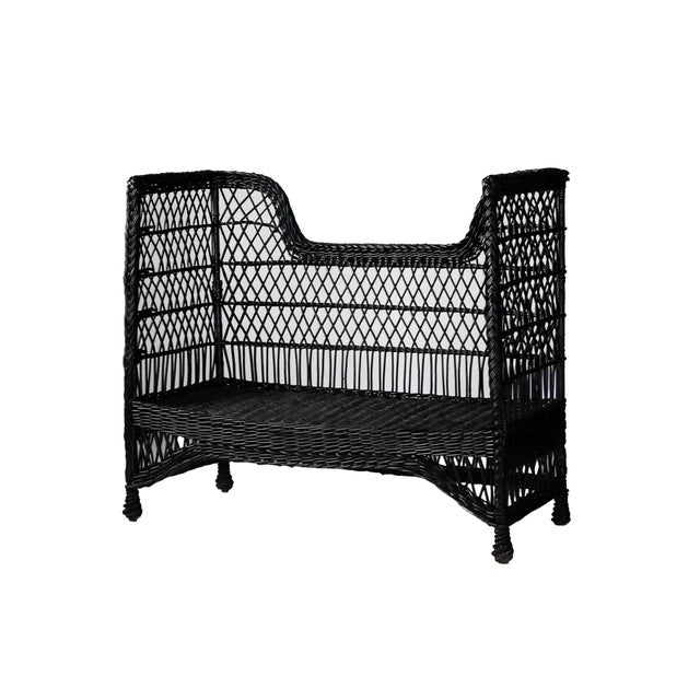 Antique black stick wicker settee, loveseat with high, flared sides, a lattice-pattern back, and blue floral patterned...
