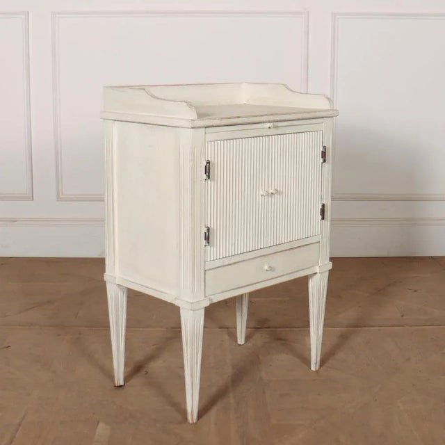 Swedish painted bedside cupboard with reeded doors. 1920. This piece is designed in the style of the selected designer...