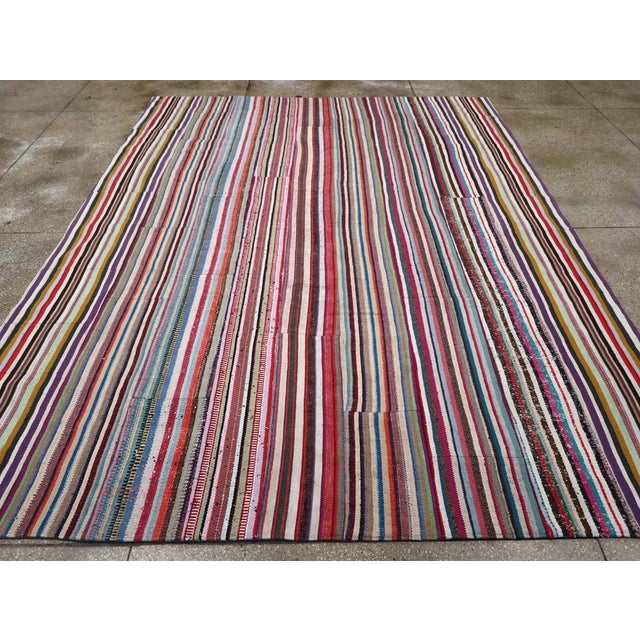 This mid-20th century Turkish flatweave Kilim rug, features a vibrant and dynamic striped design that celebrates the...
