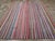 This mid-20th century Turkish flatweave Kilim rug, features a vibrant and dynamic striped design that celebrates the...