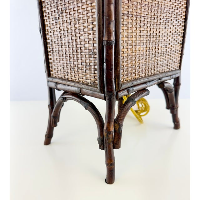 A striking vintage table lamp crafted with a dark bamboo frame surrounding tightly woven rattan panels. The tall...