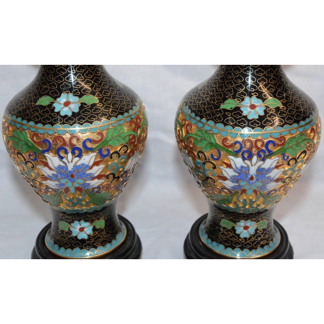 This is a colorful pair of Chinese cloisonné vases that sit atop black lacquered wooden bases. Beautiful flowers encircle...