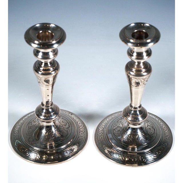 A pair of baluster-shaped candlesticks on a round, slightly stepped base, featuring an engraved band of waves running all...