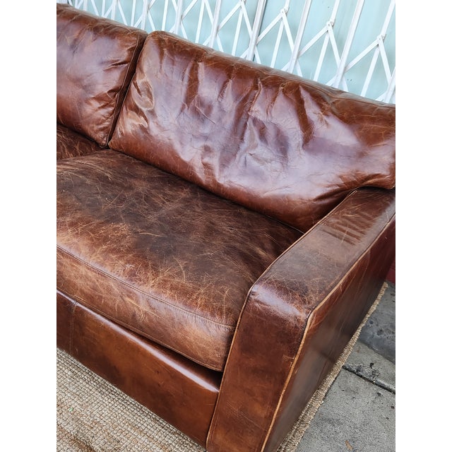Distressed brown leather sofa has a low-profile design with two large seat and back cushions. This piece is upholstered in...