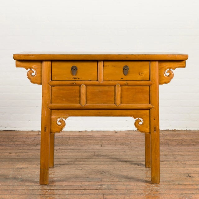 A Chinese Qing Dynasty period elm coffer table from the 19th century, with carved spandrels and drawers. Created in China...