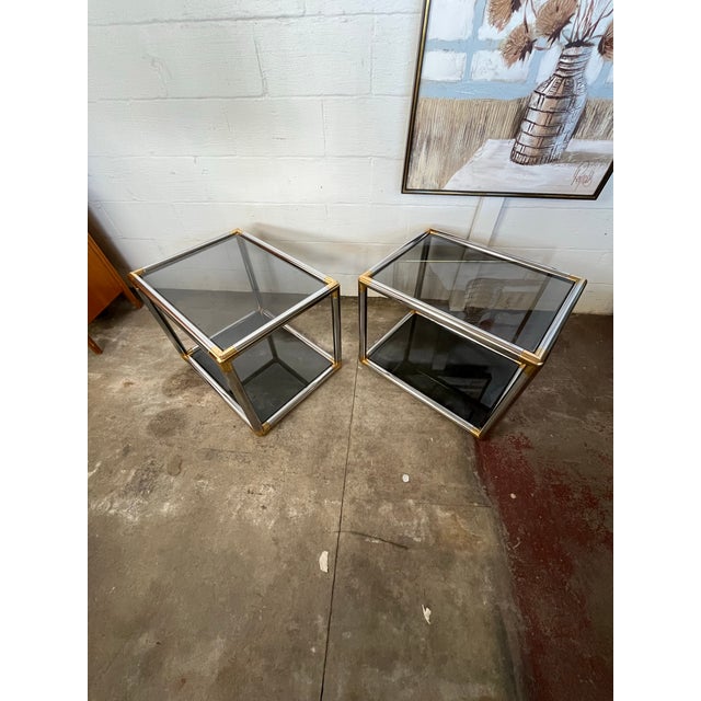 A pair of mid-20th century tubular chrome, brass and glass side or end tables, circa 1970. 2 tier with smoke glass on...