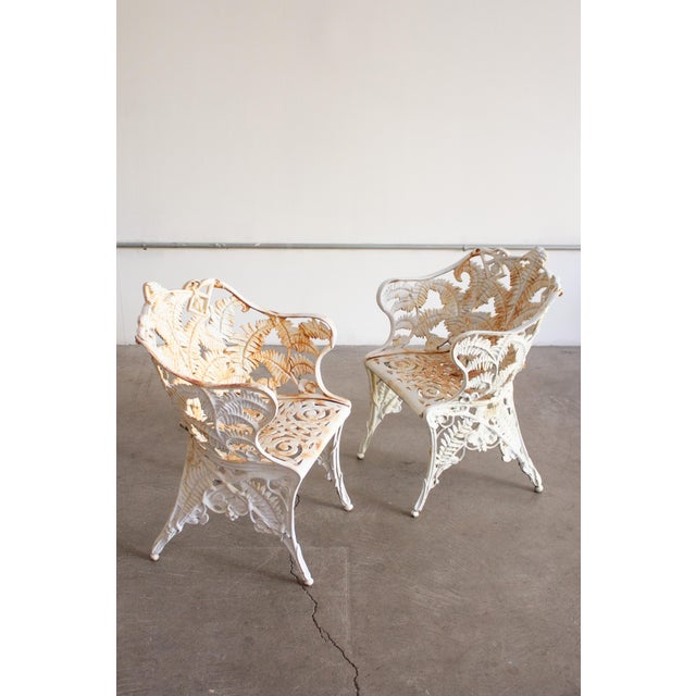 A pair of Victorian cast iron garden chairs in a “Fern” pattern. White paint with areas of rust showing though....