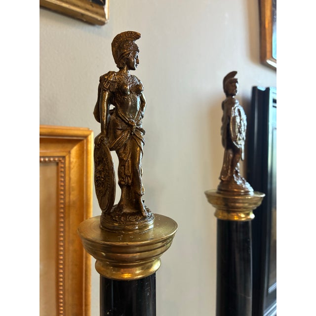 Pair of black-veined Neoclassical style architectural marble columns with a cast bronze classical warrior and the other...