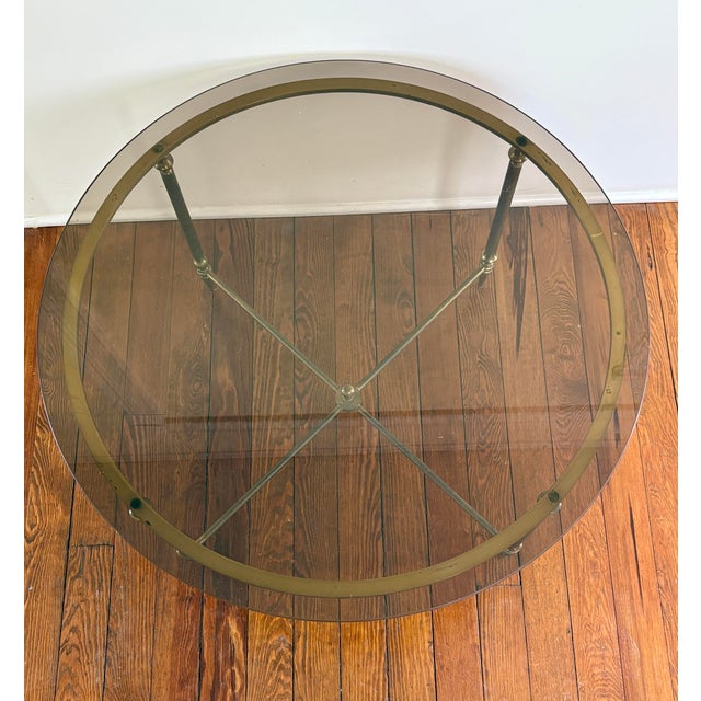 Elegant vintage round coffee table featuring a beveled glass top set within a warm brass frame. The table rests on four...