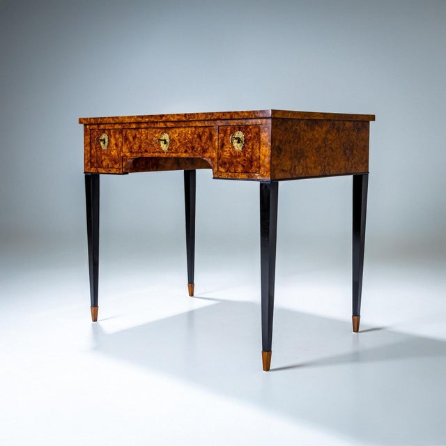 Small desk with a burlwood veneer and black lacquered writing surface. The desk stands on ebonized tapering legs and...