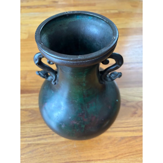 This vintage 11-inch Asian bronze amphora vessel features stylized dragon-form handles and a rich, mottled verdigris and...