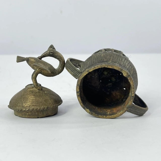 The small lidded brass bowl represents an intricate blend of artistry and commerce from centuries past, echoing the era...