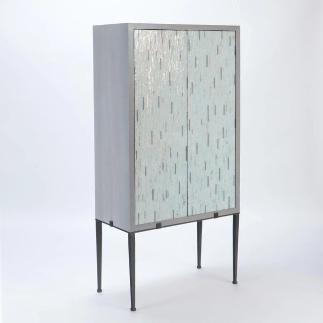A stylish custom-made cerused oak cabinet having mosaic glass doors and resting on a painted black steel frame in the...