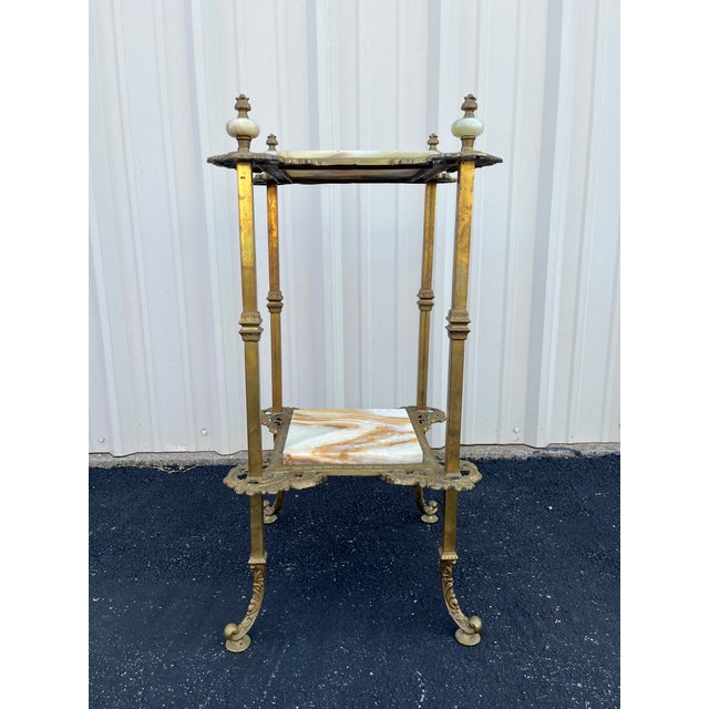 An ornate two tiered art nouveau planter stand constructed with brass and featuring polished onyx slates on each tier....