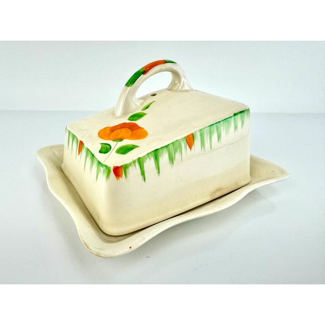 This charming butter dish, made in England, captures an artistic and whimsical essence through its hand-painted floral...