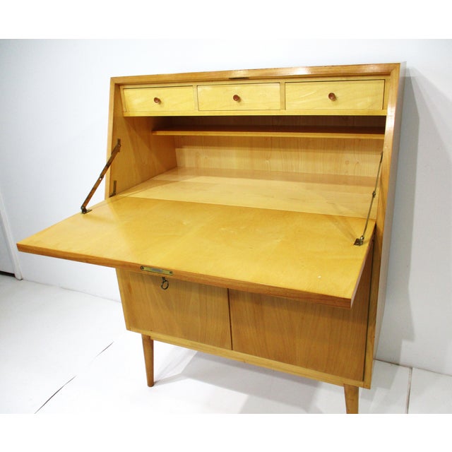 A unique secretary styled desk with locking pull down desktop with three small drawers having darker pulls and a lower...