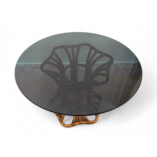 This round table features a refined sculptural base in curved, hand-woven wicker, which elegantly supports a smoked glass...