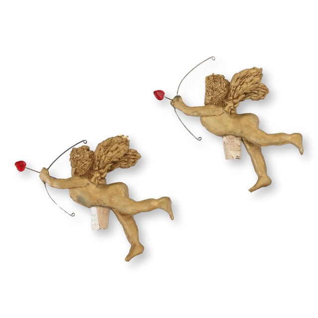 Pair of midcentury Florentine gilt cherub bottle stoppers. Each winged figure holds a bow with red glass heart arrow....