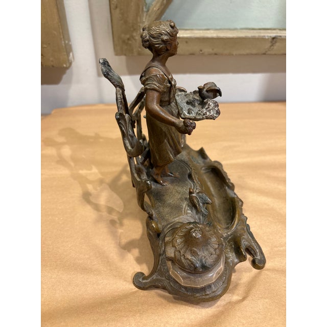 This is a beautiful antique double inkwell made of brass. It features a sculpted figure of a young woman carrying a basket...