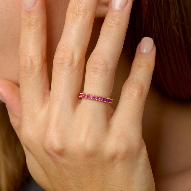This contemporary eternity band showcases a continuous row of vivid pink sapphires, each precisely set to create a...